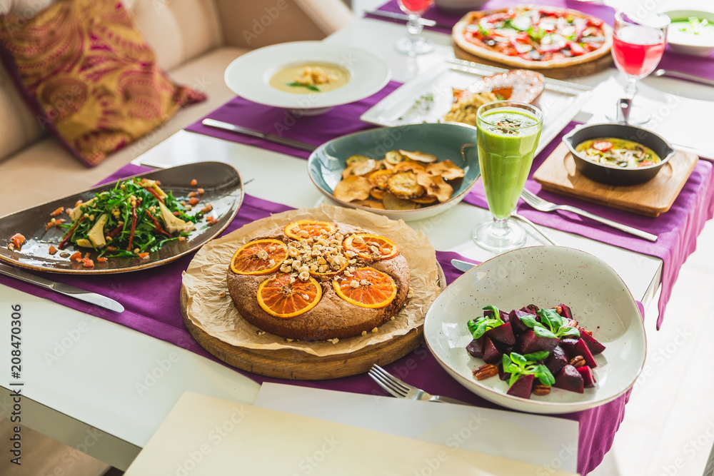Table in cafe with vegetarian dishes - pizza, salads, pie with citrus and fresh drinks.