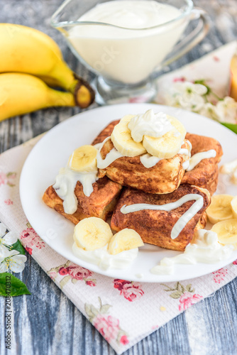 Cottage cheese pancakes in the form of cubes with banana, yogurt, honey and cherry blossom flowers on grey wooden background. Healthy breakfast food.