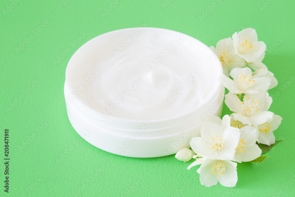 Opened jar of natural herbal cream for women on green background. Care about clean and soft face, hands, legs and body skin. Beautiful jasmine blossoms. Fresh, white flowers. Close up. Opened jar of natural herbal cream for women on green background. Care about clean and soft face, hands, legs and body skin. Beautiful jasmine blossoms. Fresh, white flowers. Close up.