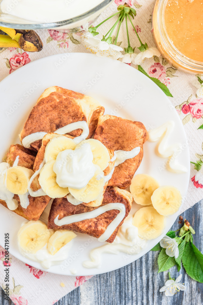 Cottage cheese pancakes in the form of cubes with banana, yogurt, honey and cherry blossom flowers on grey wooden background. Healthy breakfast food.