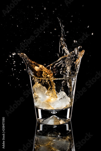 Pieces of ice fall into a glass with whiskey. A photo on a black background.