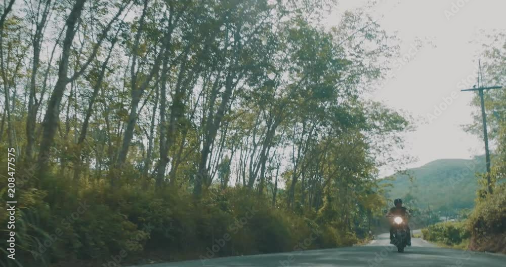Front view of cool traveler driving his chopper motorbike on tropical island road throughout forest during summerday - video in slow motion Front view of cool traveler driving his chopper motorbike on tropical island road throughout forest during summerday - video in slow motion