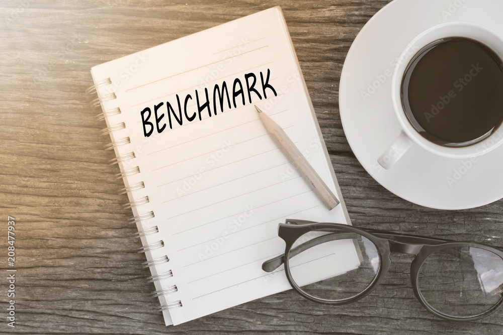 Benchmark concept on notebook with glasses, pencil and coffee cup on wooden table. Business concept. Benchmark concept on notebook with glasses, pencil and coffee cup on wooden table. Business concept.