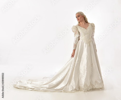 full length portrait of blonde woman wearing long white bridal gown. standing pose on white studio background.