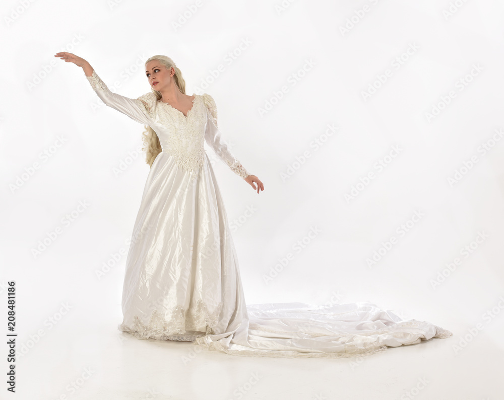 Fototapeta premium full length portrait of blonde woman wearing long white bridal gown. standing pose on white studio background.