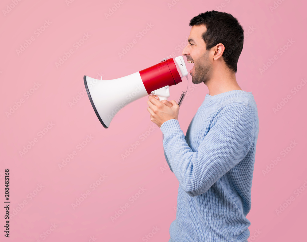 Man with blue sweater shouting through a megaphone on pink background Man with blue sweater shouting through a megaphone on pink background