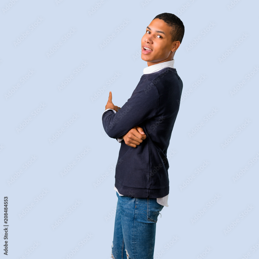 Young african american man pointing back with the index finger on isolated blue background Young african american man pointing back with the index finger on isolated blue background