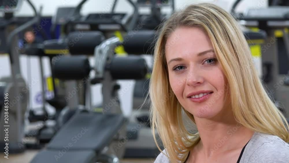 A young beautiful woman smiles at the camera in a gym A young beautiful woman smiles at the camera in a gym