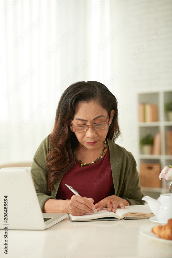 Serious mature woman making notes in her notebook Serious mature woman making notes in her notebook