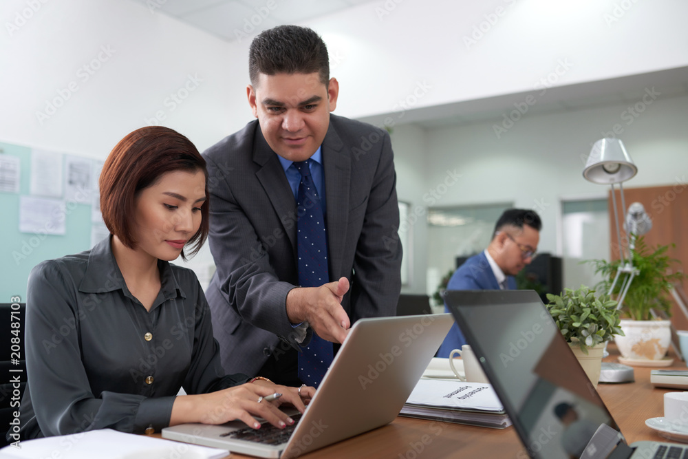 Multi-ethnic team of white collar workers working on joint project while gathered together at spacious boardroom Multi-ethnic team of white collar workers working on joint project while gathered together at spacious boardroom