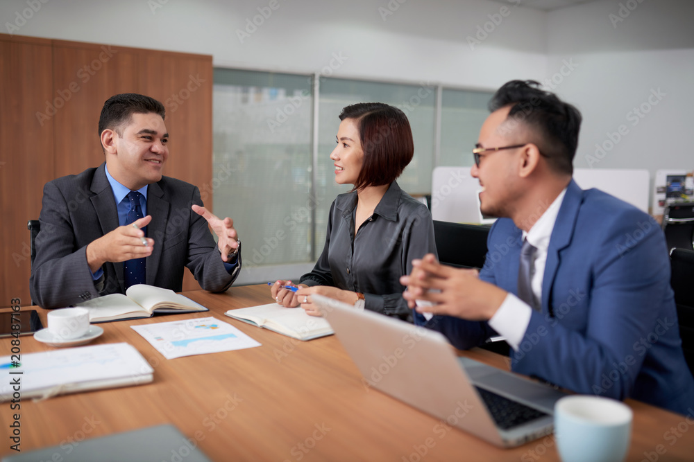 Multi-ethnic team of managers gathered together at spacious meeting room and sharing creative ideas concerning start-up project with each other Multi-ethnic team of managers gathered together at spacious meeting room and sharing creative ideas concerning start-up project with each other