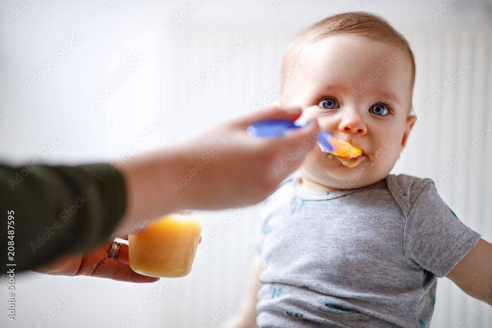 Mother feeds baby with fruit porridge - obrazy, fototapety, plakaty 