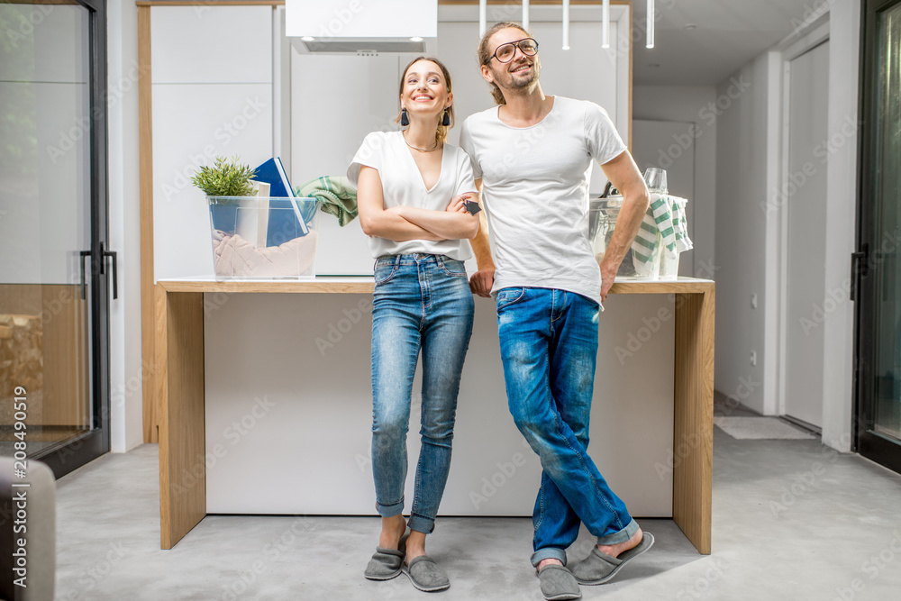 Young and happy couple enjoying their new modern apartment standing at the kitchen with different home stuff on the background Young and happy couple enjoying their new modern apartment standing at the kitchen with different home stuff on the background