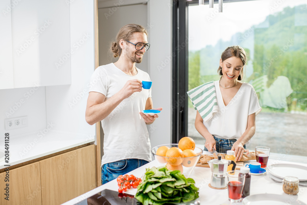 Young couple cooking breakfast with healthy food and coffee standing at the modern kitchen interior