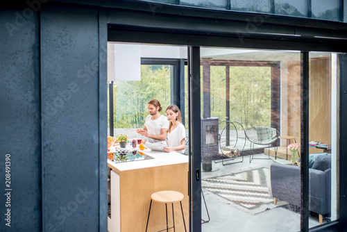 View through the window on the modern house interior with young couple eating indoors