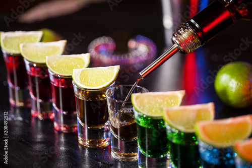 Photos Bartender pouring alcoholic drink into small glasses on bar
