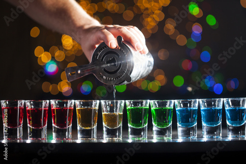 Bartender pouring alcoholic drink into small glasses on bar. Colorful cocktails at the bar.