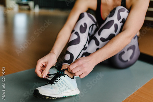 The hands of the girl tying shoelaces at gym. Woman on a mat getting ready for fitness. Concept of sport training. front view.