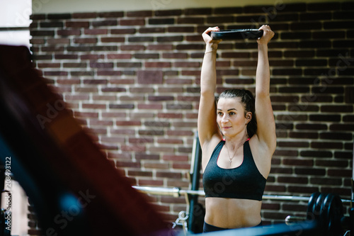 The girl holds a metal round weights plate  dumbbell in her hands above her head. Portrait of strong sporty woman doing exercise in gym. sport  fitness  lifestyle.