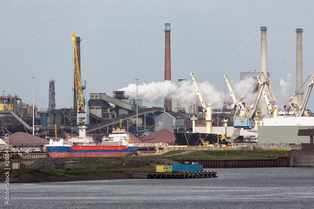 Fototapeta premium Big steel factory in harbor IJmuiden with cargo carrier in front, The Netherlands