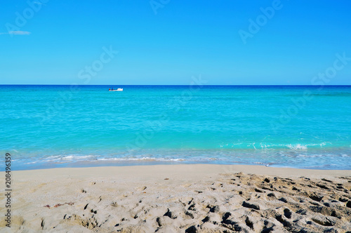 coastline of the ocean  small waves  horizon  endless distance  white motor boat with silhouettes of people in the ocean  against a blue sky covered with sparse clouds Cuba