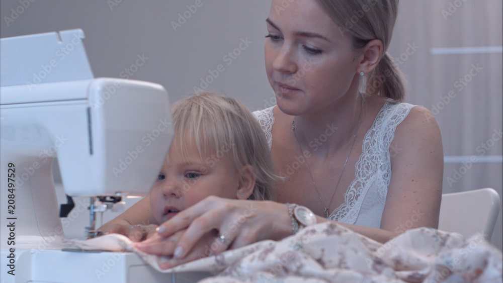 Small child learns new knowledge with her mother using sewing machine