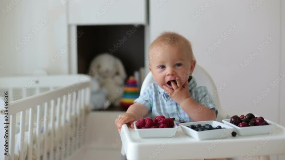 Adorable little baby boy, eating fresh fruits at home, sitting in baby chair in kids room Adorable little baby boy, eating fresh fruits at home, sitting in baby chair in kids room