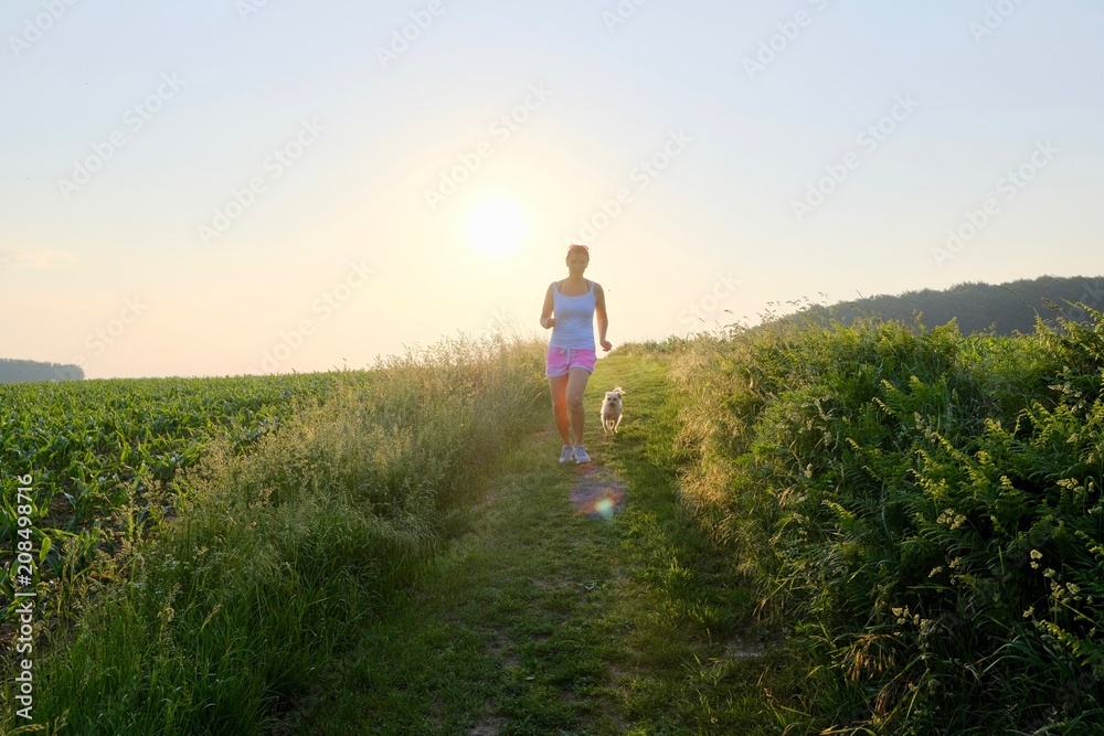 Woman Silhouette with a dog running down a gravel path at sunset