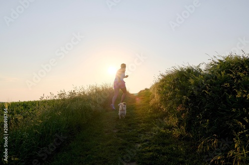 Woman Silhouette with a dog running up a gravel path at sunset
