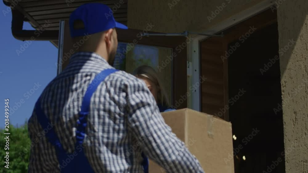 Mail courier giving tablet to young woman for signing and delivering big carton box at home porch Mail courier giving tablet to young woman for signing and delivering big carton box at home porch