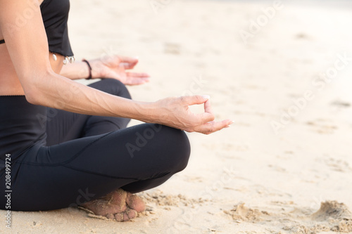 Slim mature woman in black practicing yoga on sand beach