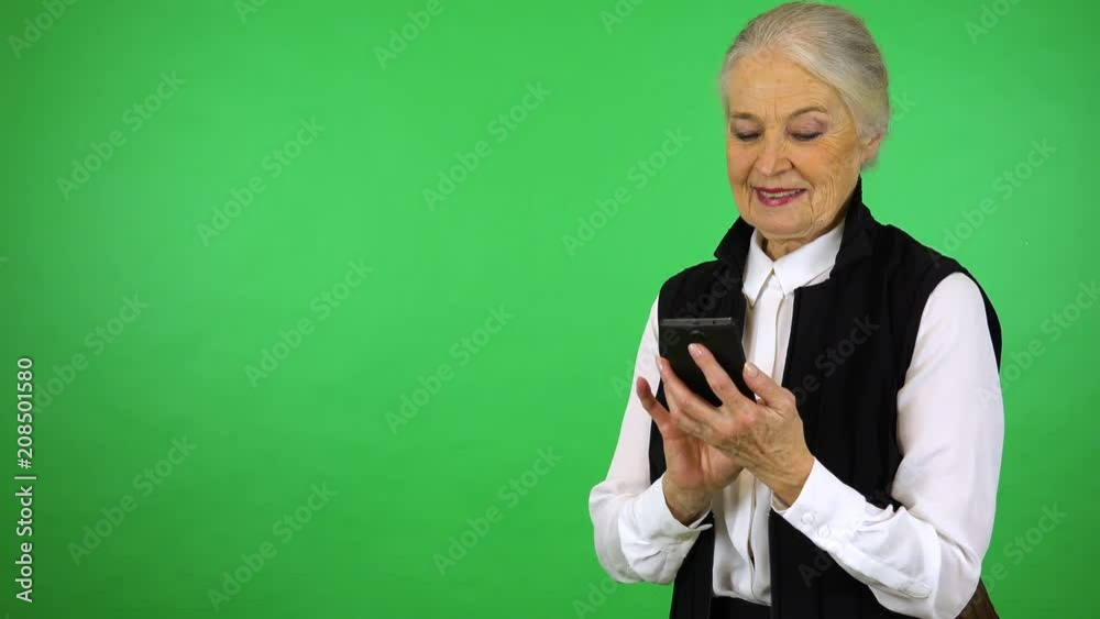 An elderly woman works on a smartphone with a smile - green screen studio An elderly woman works on a smartphone with a smile - green screen studio