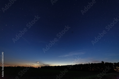 Bright star-planet Venus over the field and forest against the starry sky at dusk.