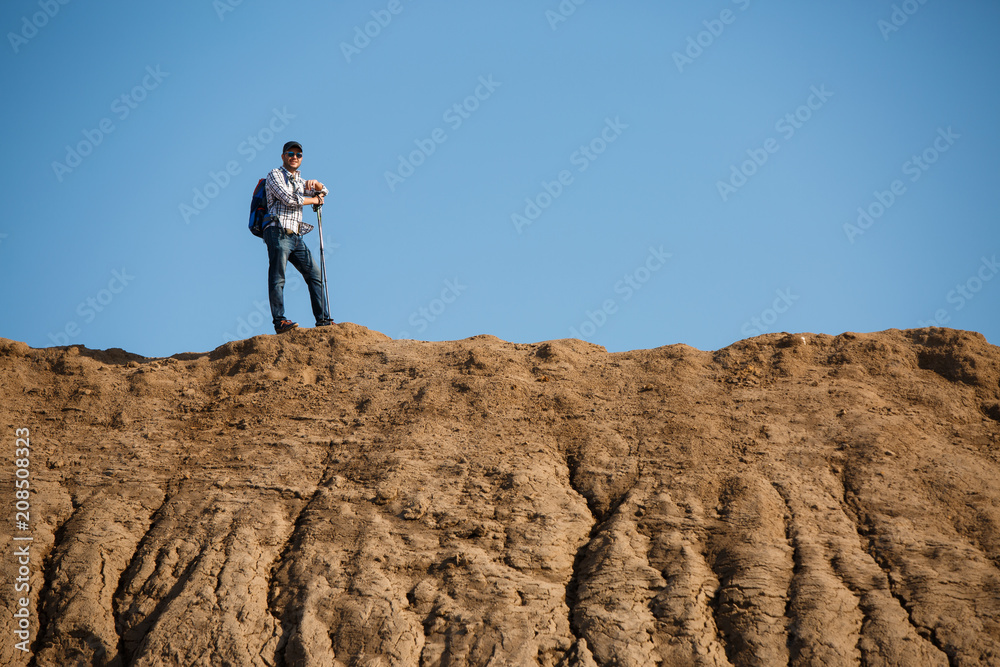 Image of afar of tourist man with sticks for walking on hill against blue sky