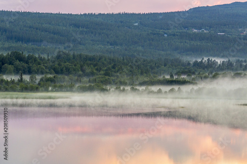Fog over a forest lake at sunset and reflections in the water