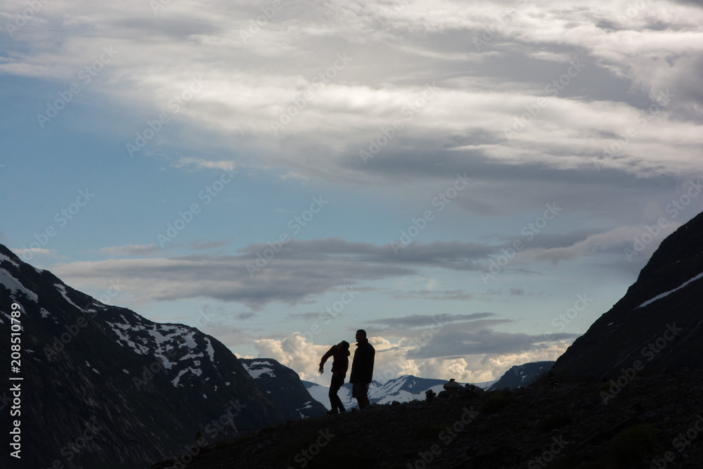 Two men throwing rocks among mountains in the sunset