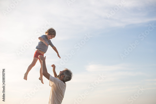 Happy Dad Tossing Son into Air on Beach in Summer on Vacation