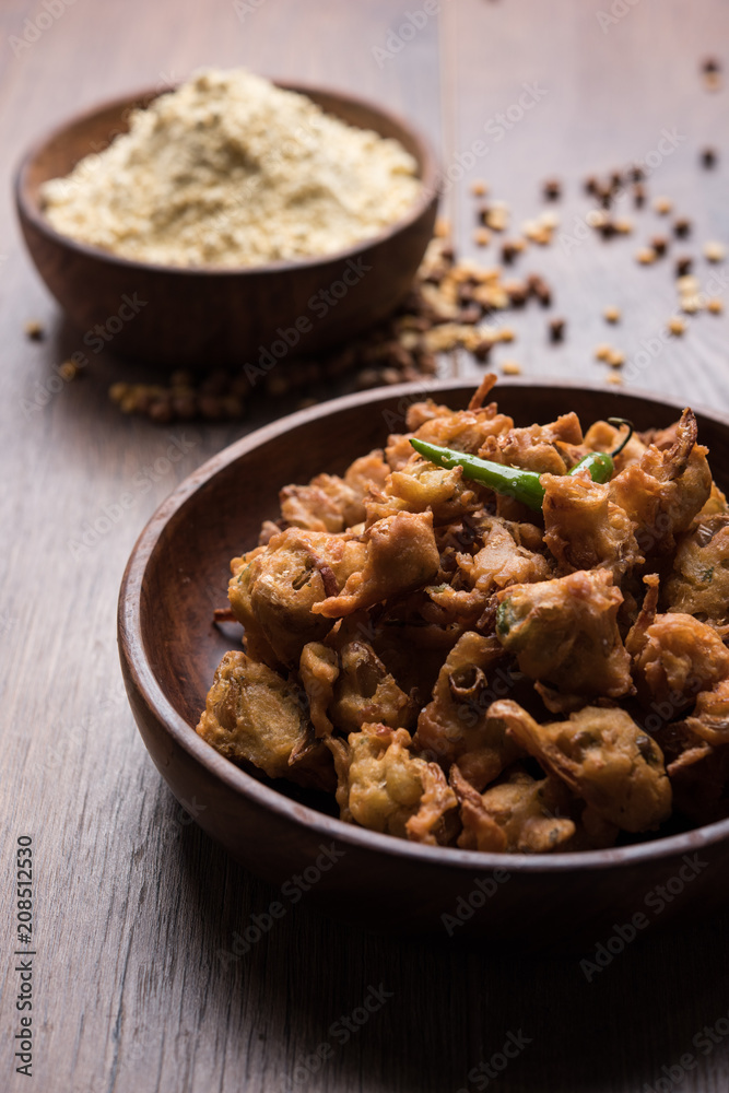Chick pea flour or Besan powder in a ceramic or wooden bowl along with fried onion pakora or kanda bajji Chick pea flour or Besan powder in a ceramic or wooden bowl along with fried onion pakora or kanda bajji