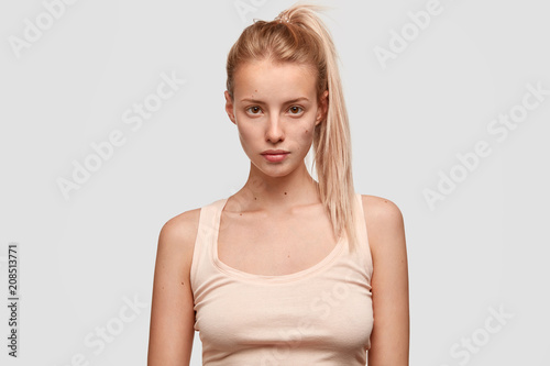 Indoor view of pleasant looking sportswoman with pony tail, dressed in casual t shirt, rests indoor after jogging, has confident expression, isolated over white background. People, lifestyle concept