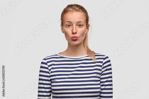Lovely young female pouts lips and has appealing appearance, dressed in sailor casual sweater, spends leisure time in family circle, isolated over white background. People and facial expressions
