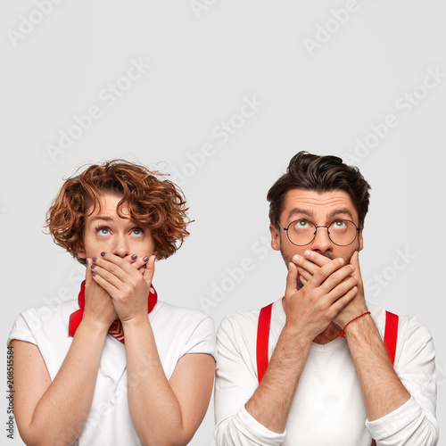 Isolated shot of stunned curly female and her business partner see something unbelievable, cover mouth with hands, being shocked to notice leaking ceiling, pose against white background, blank space