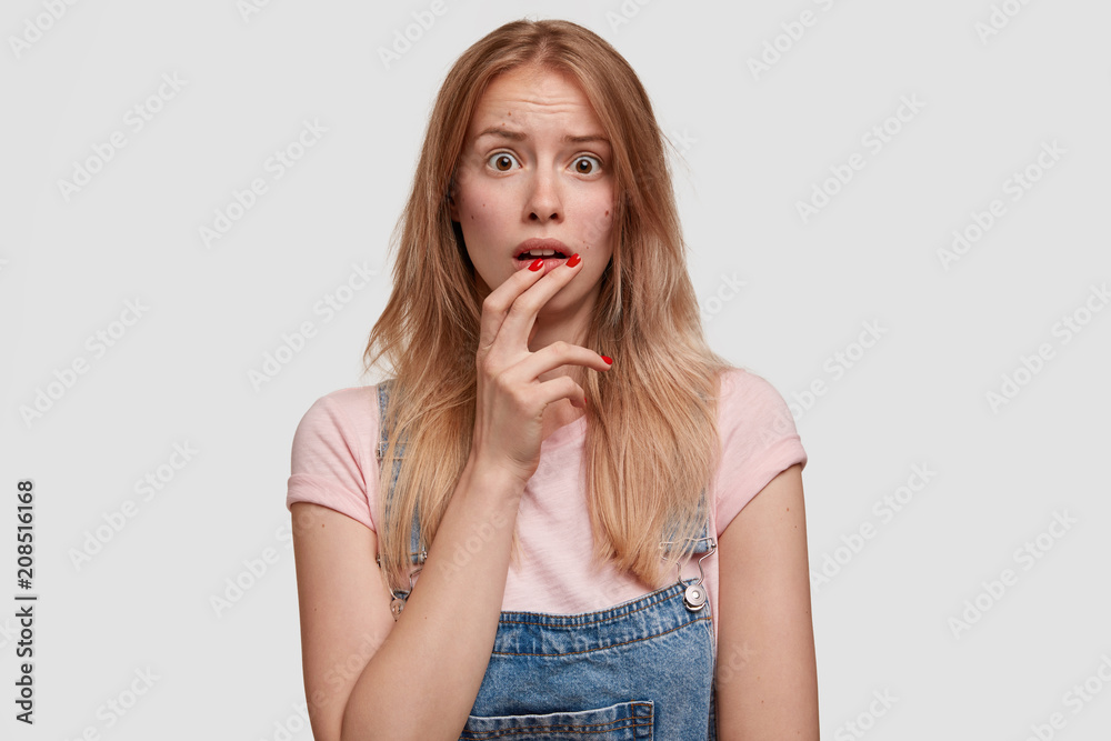 Cute frightened European woman looks with puzzled expression, recieves bad news from relatives, has wide opened eyes in stupor, poses against white studio background. People and reaction concept Cute frightened European woman looks with puzzled expression, recieves bad news from relatives, has wide opened eyes in stupor, poses against white studio background. People and reaction concept