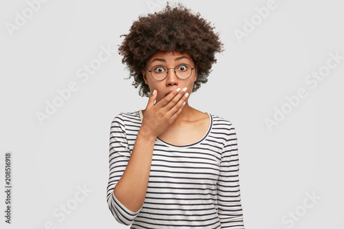 People and diversity concept. Lovely young African American female looks with frightened expression, stares with eyes popped out, sees sudden accident on road, has bated breath, dressed casually