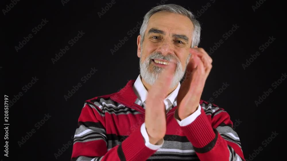 An elderly man applauds and smiles at the camera - black screen studio An elderly man applauds and smiles at the camera - black screen studio