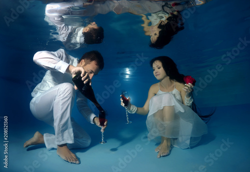 Bride and groom drink red wine underwater in the pool. Underwater wedding photo