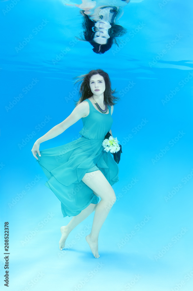 Young beautiful woman in a pale blue dress with a bouquet of flowers posing under water (for the calendar, spring, March)