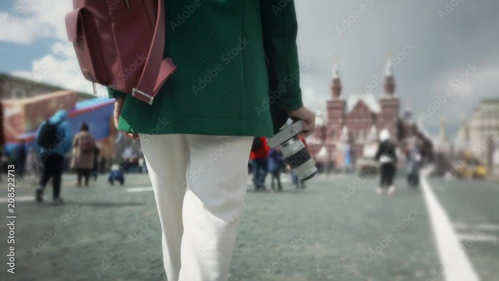 Rear view of a young unrecognizable woman in casual clothes walking in Moscow near Kremlin holding camera in her hand. Tourism concept. Tracking medium shot Rear view of a young unrecognizable woman in casual clothes walking in Moscow near Kremlin holding camera in her hand. Tourism concept. Tracking medium shot
