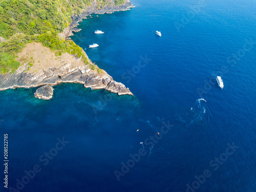 Aerial drone view of a remote tropical island surrounded by coral reef and several diving boats