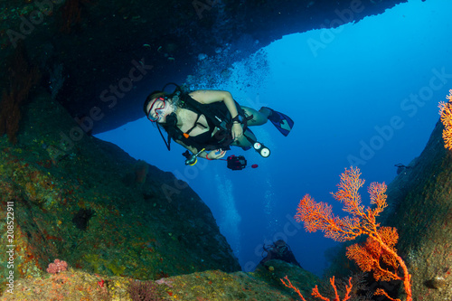 Female SCUBA diver swimming through an underwater tunnel on a tropical coral reef