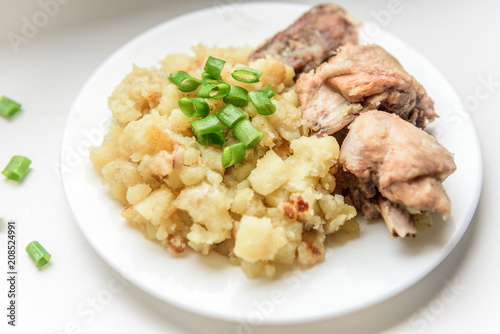 Stewed potatoes with chicken and green onions on white plate.